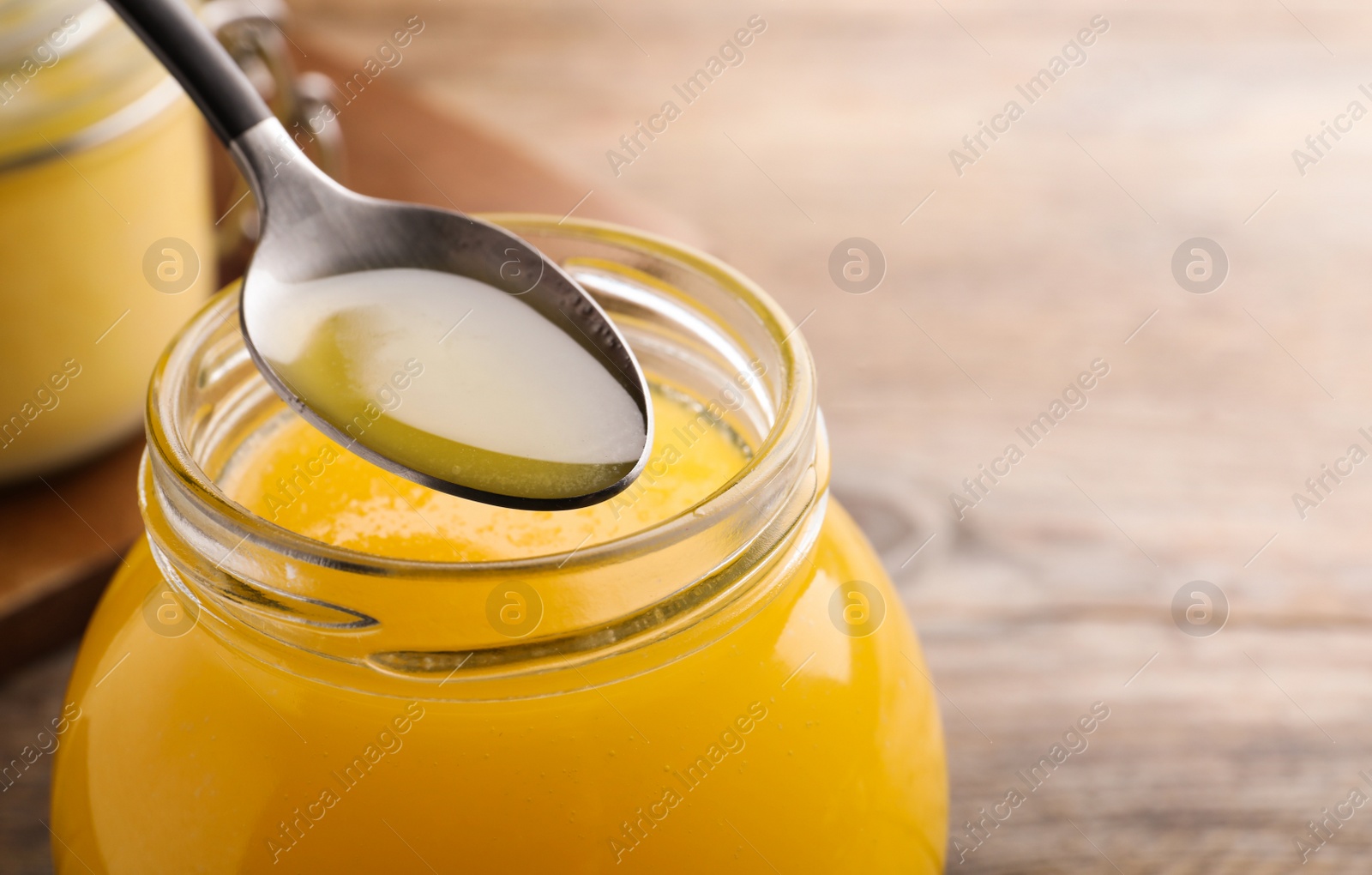 Photo of Glass jar and spoon of Ghee butter on wooden table, closeup. Space for text