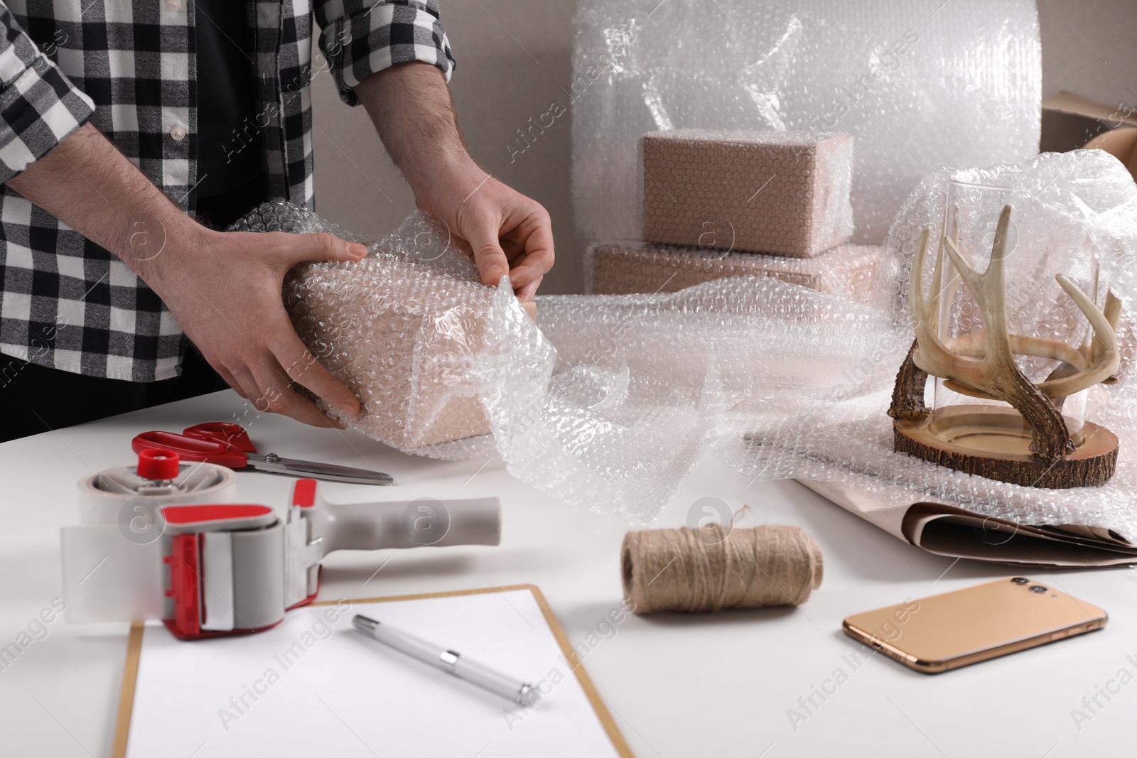 Photo of Man covering box with bubble wrap at table in warehouse, closeup