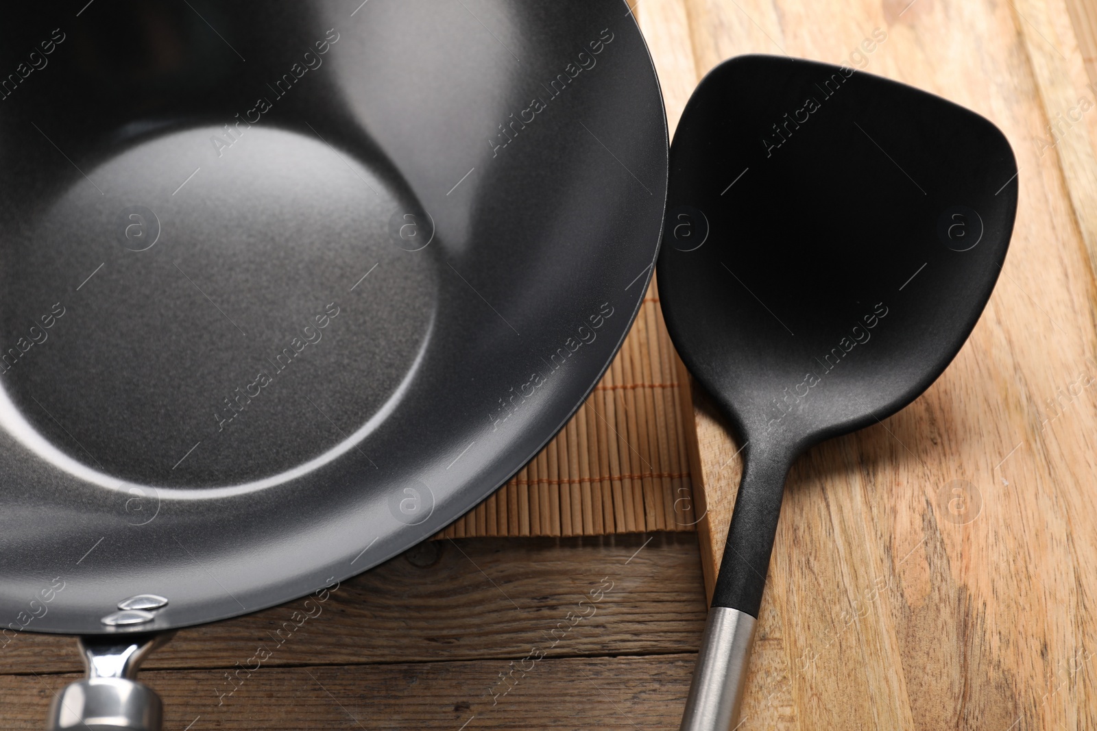 Photo of Black metal wok and spatula on wooden table, closeup