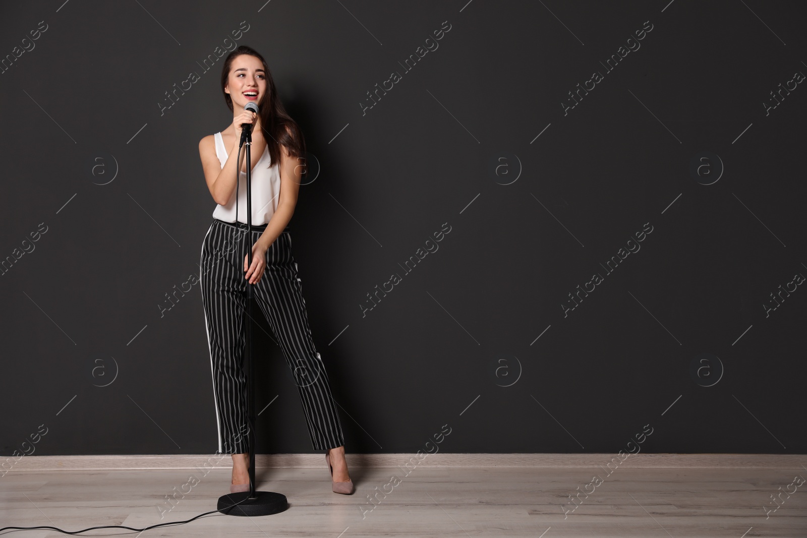 Photo of Young stylish woman singing in microphone near dark wall. Space for text