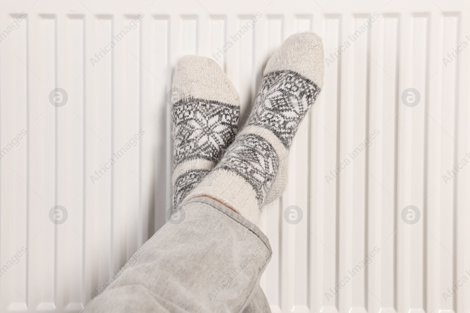 Photo of Woman warming feet near heating radiator, closeup