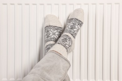 Woman warming feet near heating radiator, closeup