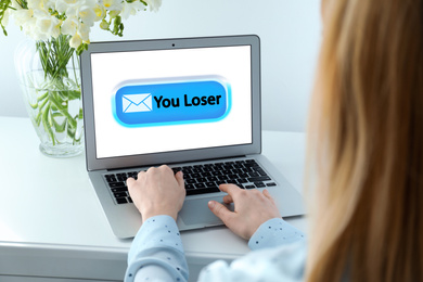 Young woman using laptop at white table, closeup. Cyber bullying