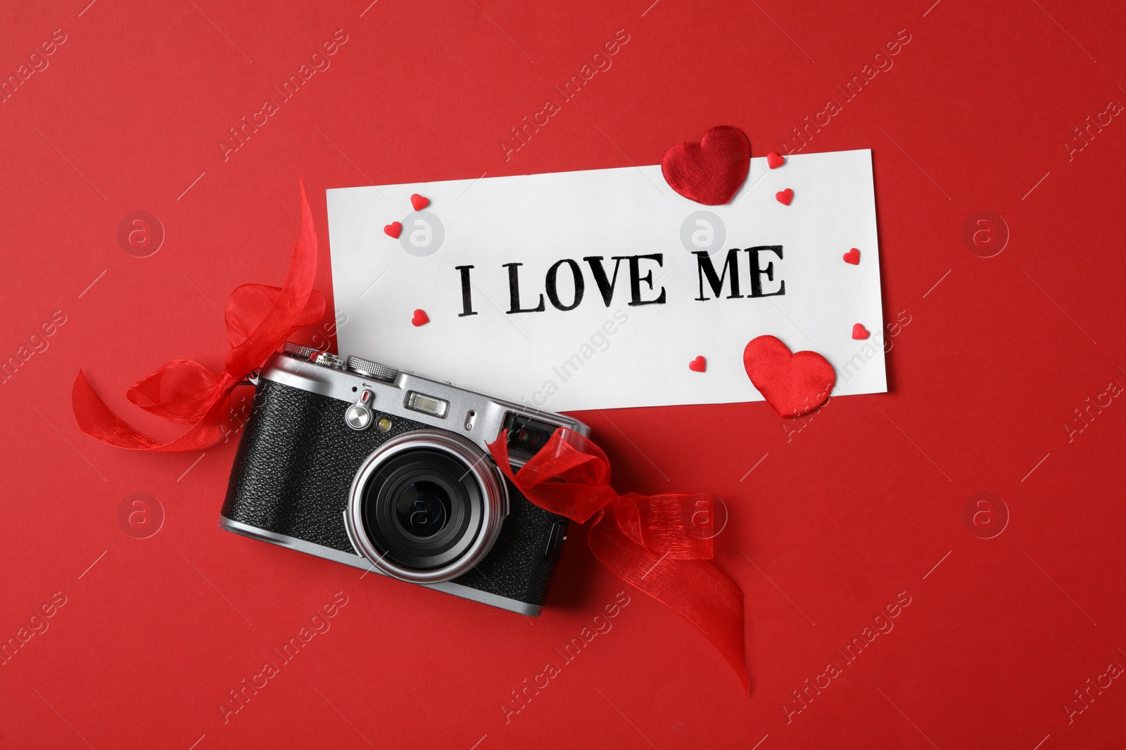 Photo of Paper with handwritten phrase I Love Me, camera and hearts on red background, flat lay