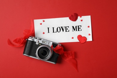 Photo of Paper with handwritten phrase I Love Me, camera and hearts on red background, flat lay