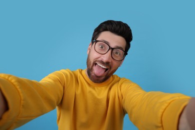 Smiling man showing tongue while taking selfie on light blue background