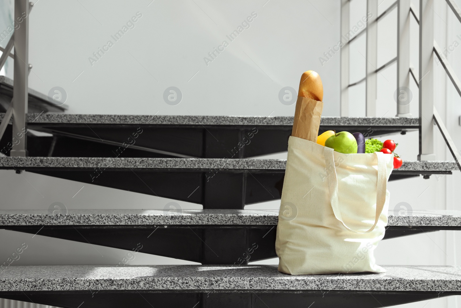 Photo of Tote bag with vegetables and bread on stairs indoors. Space for text