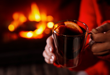 Photo of Woman with tasty mulled wine near burning fireplace indoors, closeup