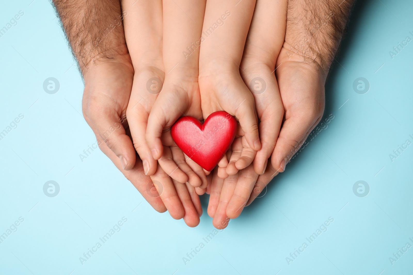 Photo of Parents and kid holding red heart in hands on light blue background, top view