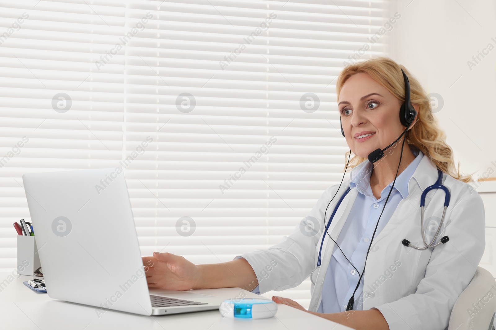 Photo of Doctor with laptop and headphones consulting patient in clinic. Online medicine concept