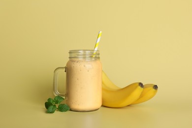Photo of Mason jar with tasty smoothie, mint leaves and bananas on beige background
