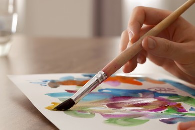 Woman painting with watercolor at wooden table indoors, closeup