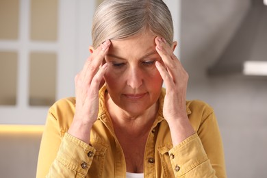 Photo of Menopause. Woman suffering from headache in kitchen