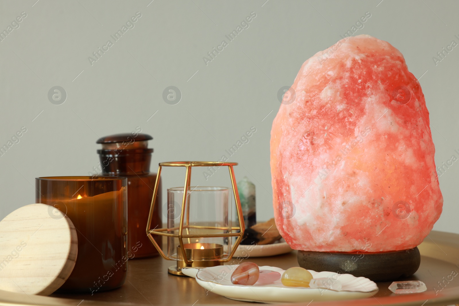 Photo of Himalayan salt lamp, candles and crystals on golden table near light grey wall