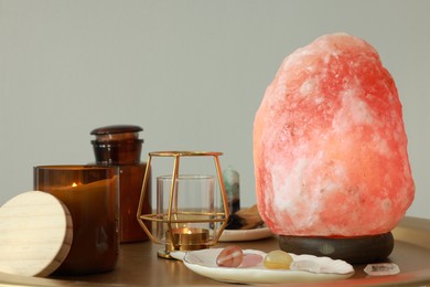 Himalayan salt lamp, candles and crystals on golden table near light grey wall