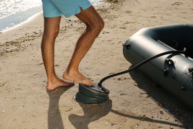 Photo of Man pumping inflatable rubber fishing boat at sandy beach on sunny day, closeup