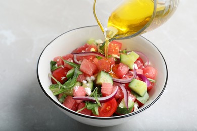 Photo of Adding olive oil to delicious salad with watermelon, vegetables and feta cheese at light table