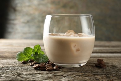 Coffee cream liqueur in glass, mint and beans on wooden table, closeup