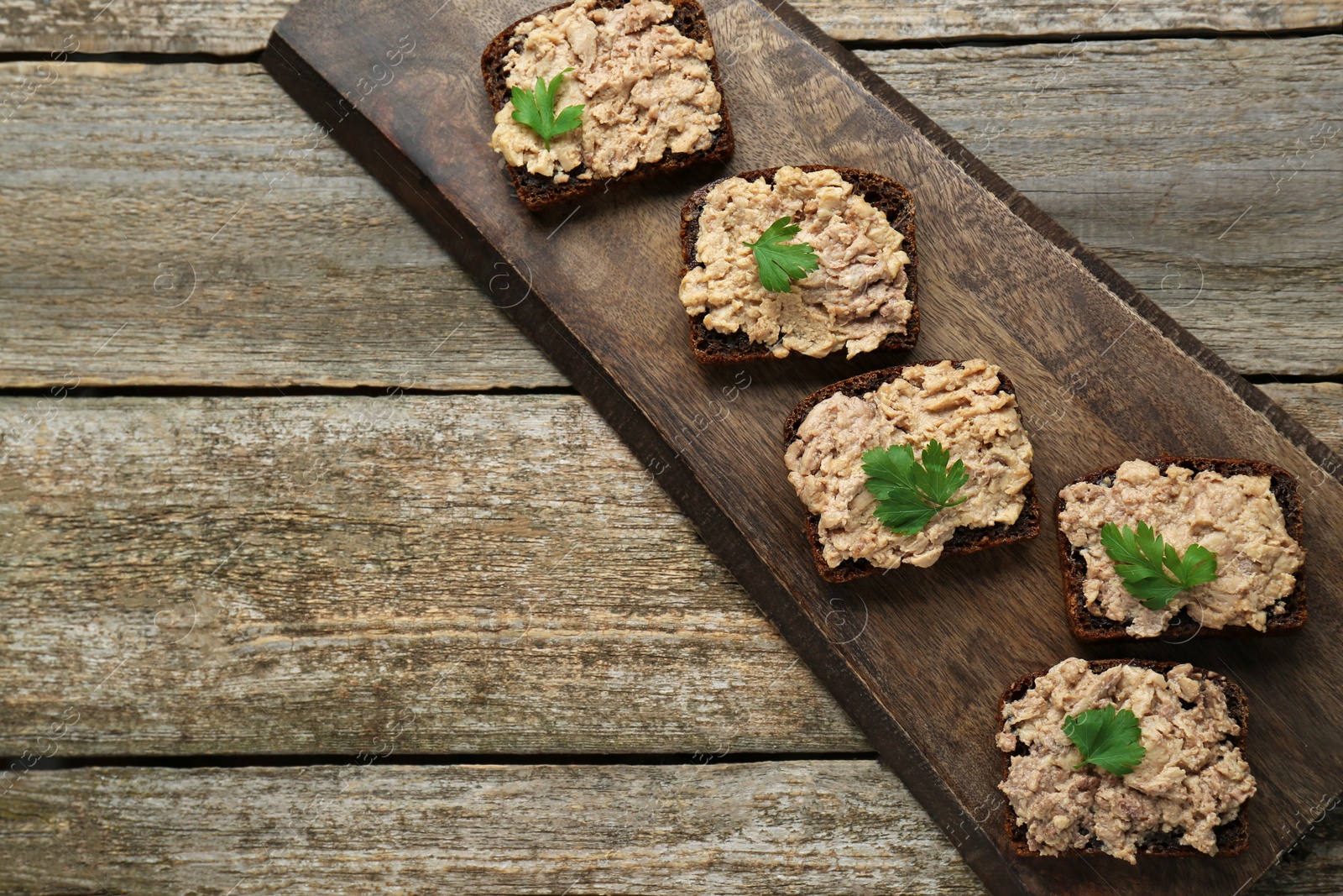 Photo of Tasty sandwiches with cod liver and parsley on wooden table, top view. Space for text