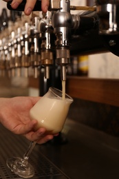 Photo of Bartender pouring fresh beer into glass in pub, closeup