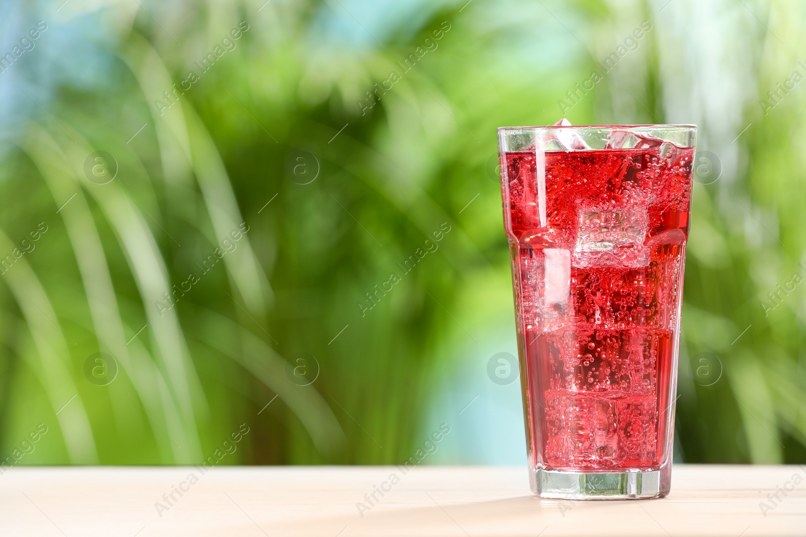 Photo of Glass of refreshing soda water with ice cubes on white table outdoors, space for text