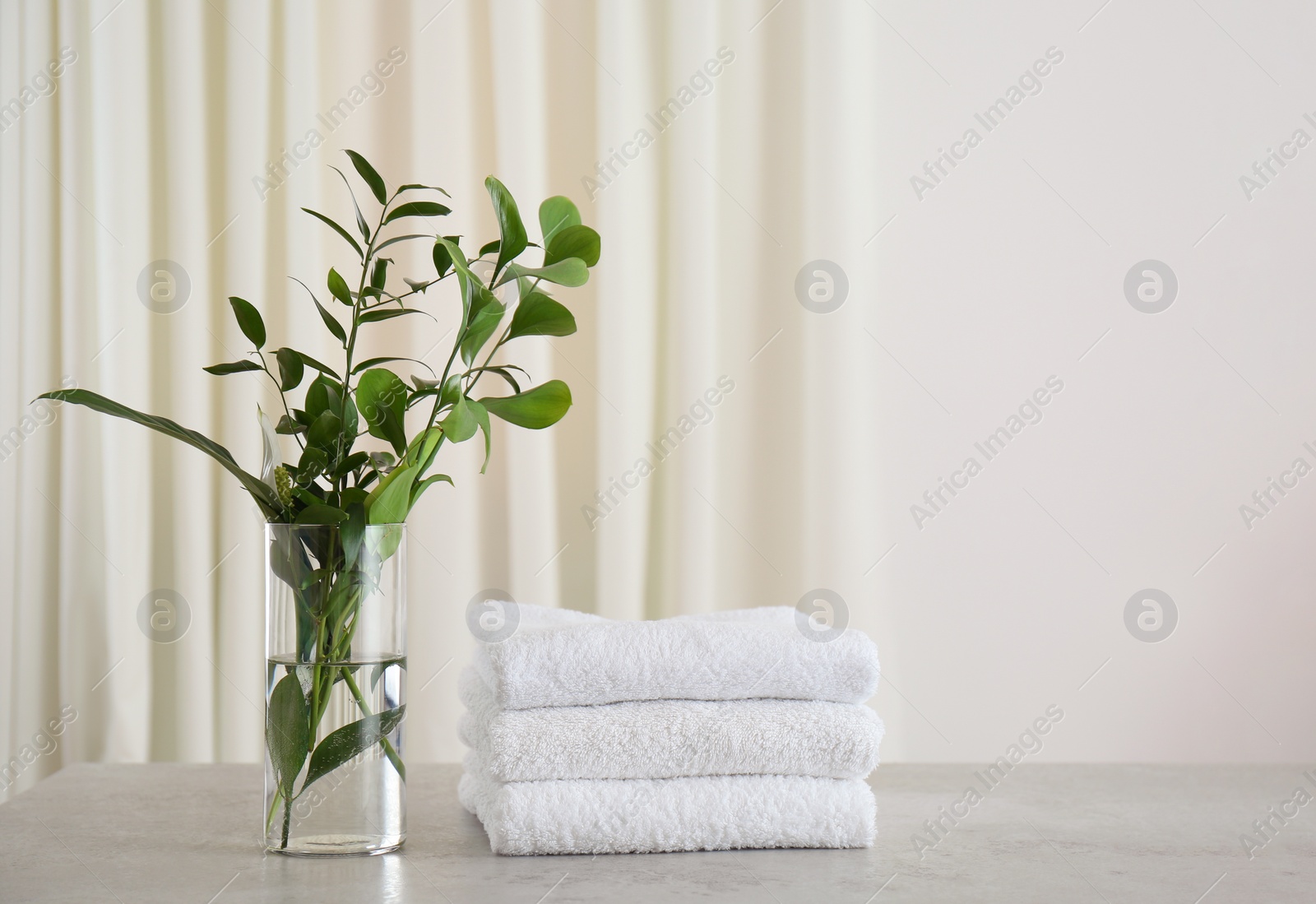 Photo of Fresh towels and green branches on light grey stone table in bathroom