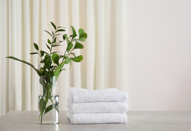 Photo of Fresh towels and green branches on light grey stone table in bathroom