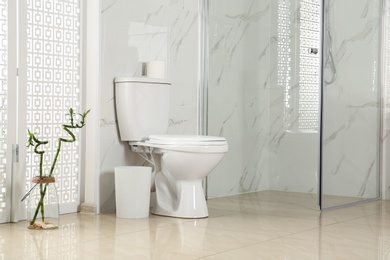 Photo of Toilet bowl near shower stall in modern bathroom interior