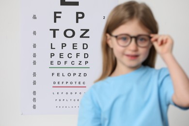 Photo of Little girl with glasses against vision test chart, selective focus