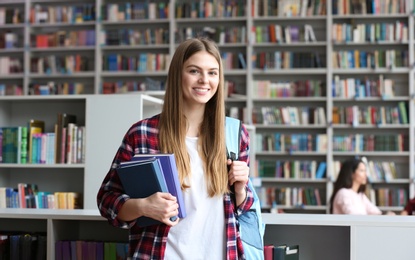 Young pretty woman with books and backpack in library. Space for text