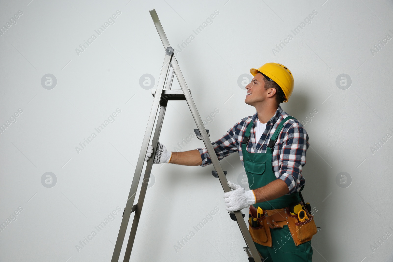 Photo of Professional builder with metal ladder on light background