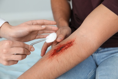 Photo of Female doctor cleaning young man's arm injury in clinic, closeup. First aid