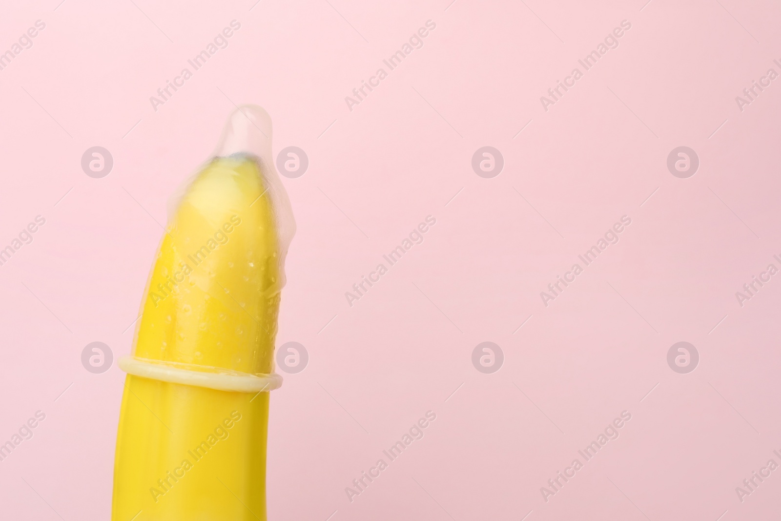Photo of Banana with condom on pink background, closeup and space for text. Safe sex concept