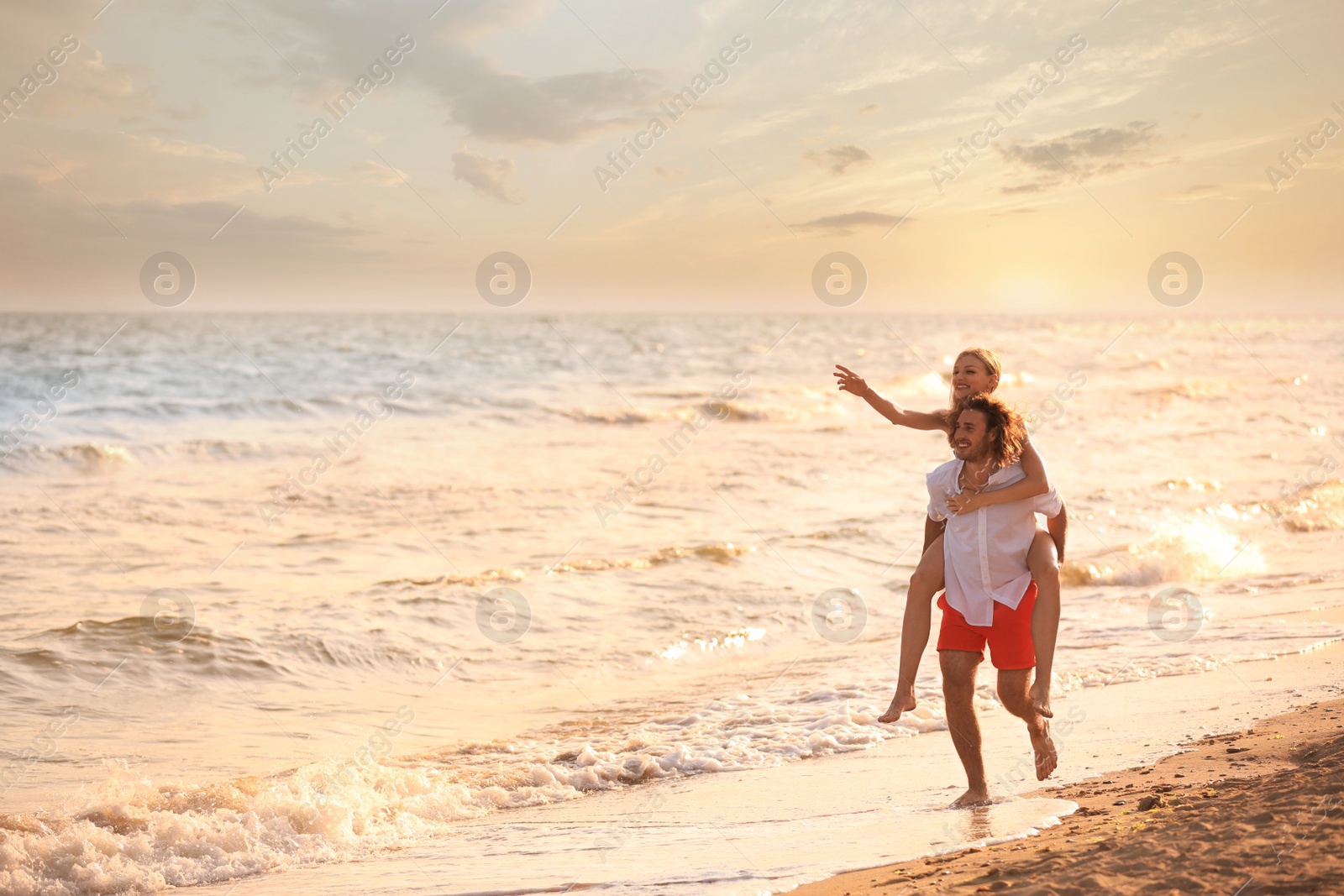 Photo of Young woman in bikini and her boyfriend having fun on beach at sunset. Lovely couple