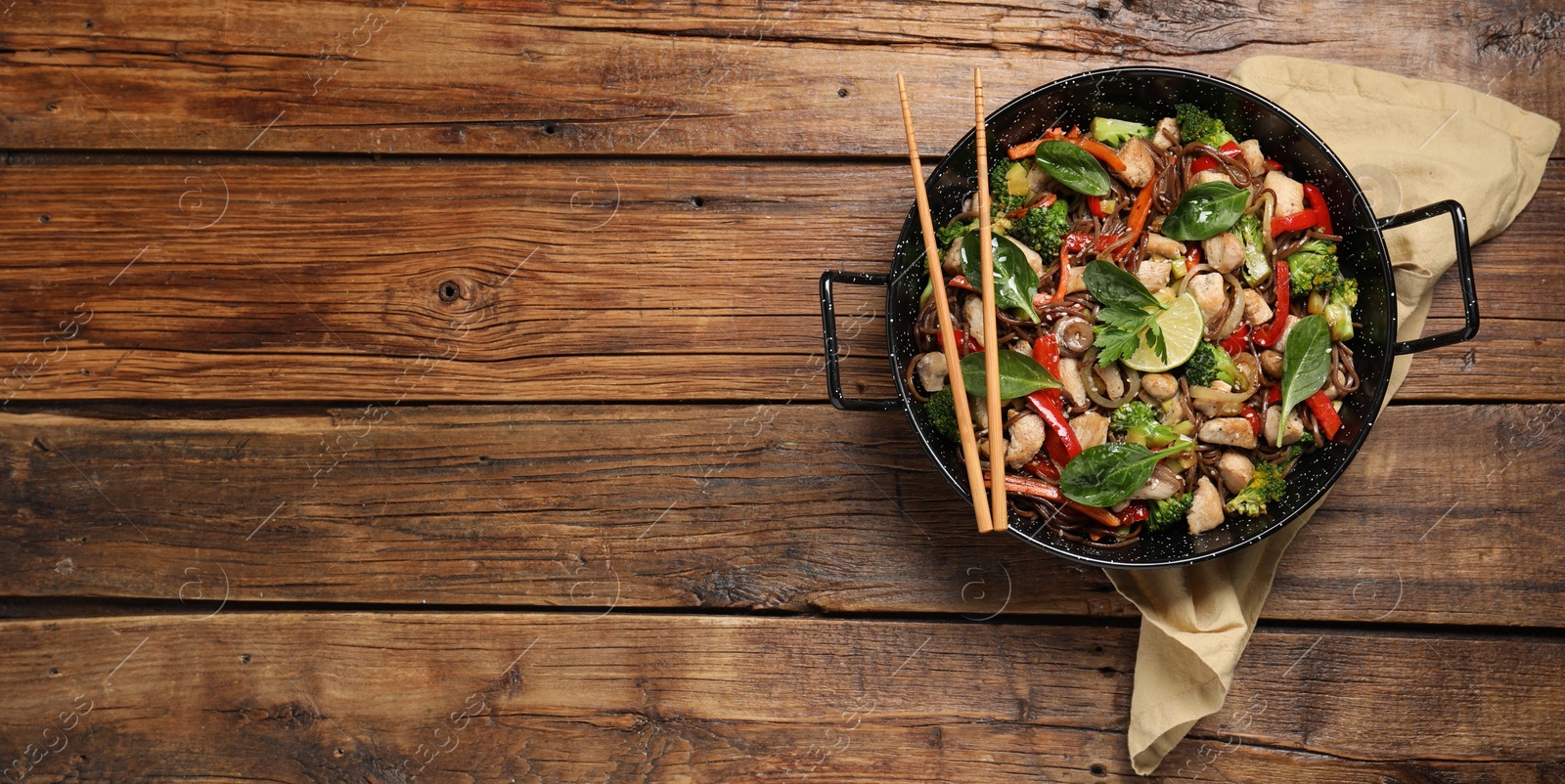 Photo of Stir-fry. Tasty noodles with meat in wok and chopsticks on wooden table, top view. Space for text