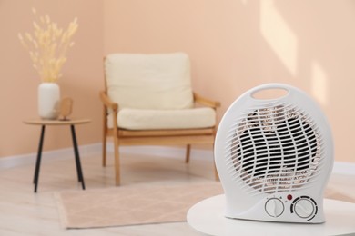 Photo of Compact electric fan heater on white table indoors. Space for text