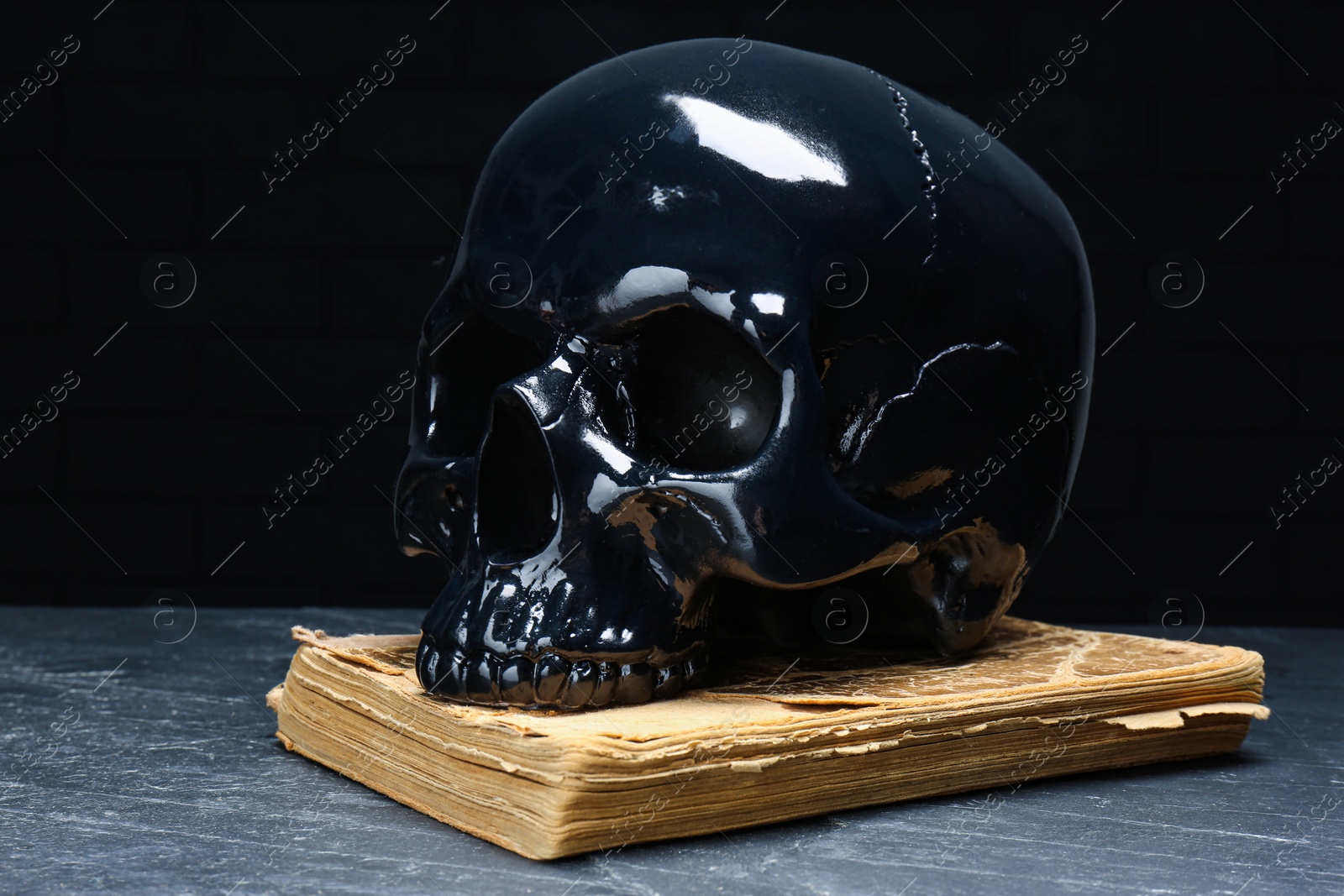 Photo of Glossy skull with book on dark grey table, closeup