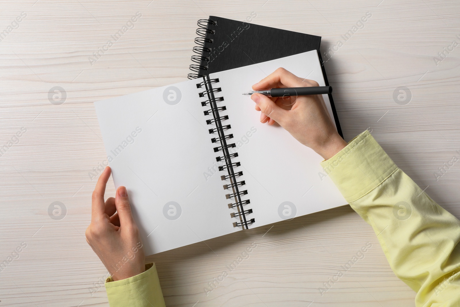 Photo of Woman writing in notebook at white wooden table, top view