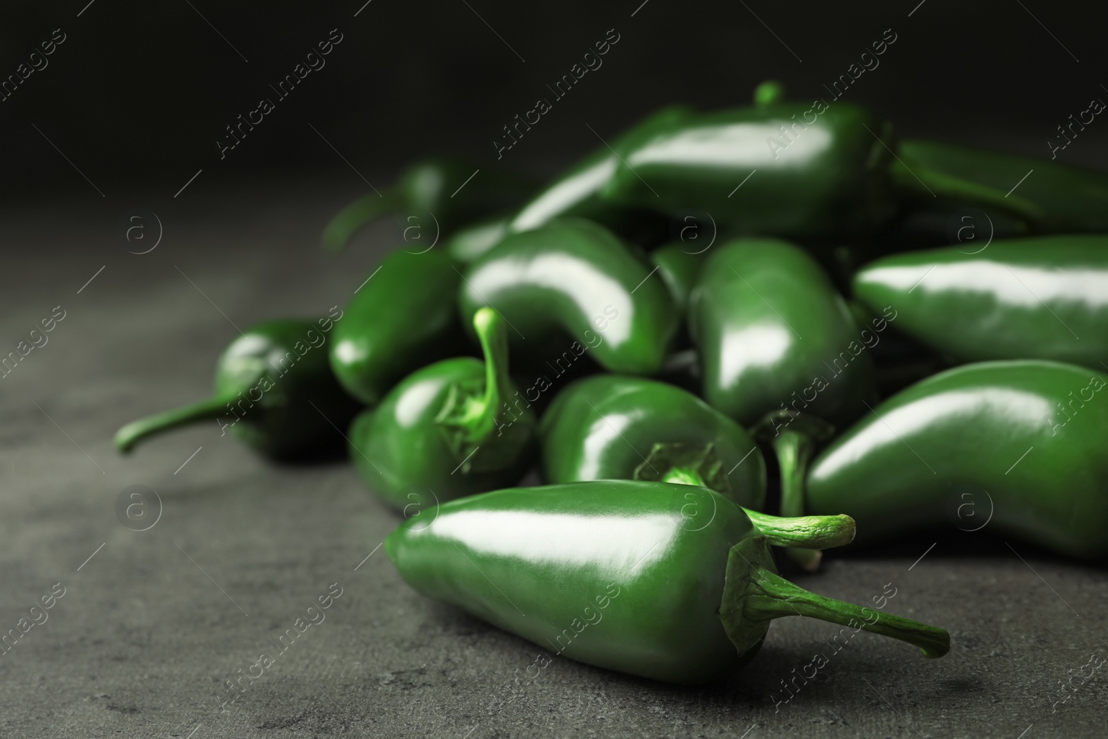 Photo of Pile of green hot chili peppers on grey table, closeup. Space for text