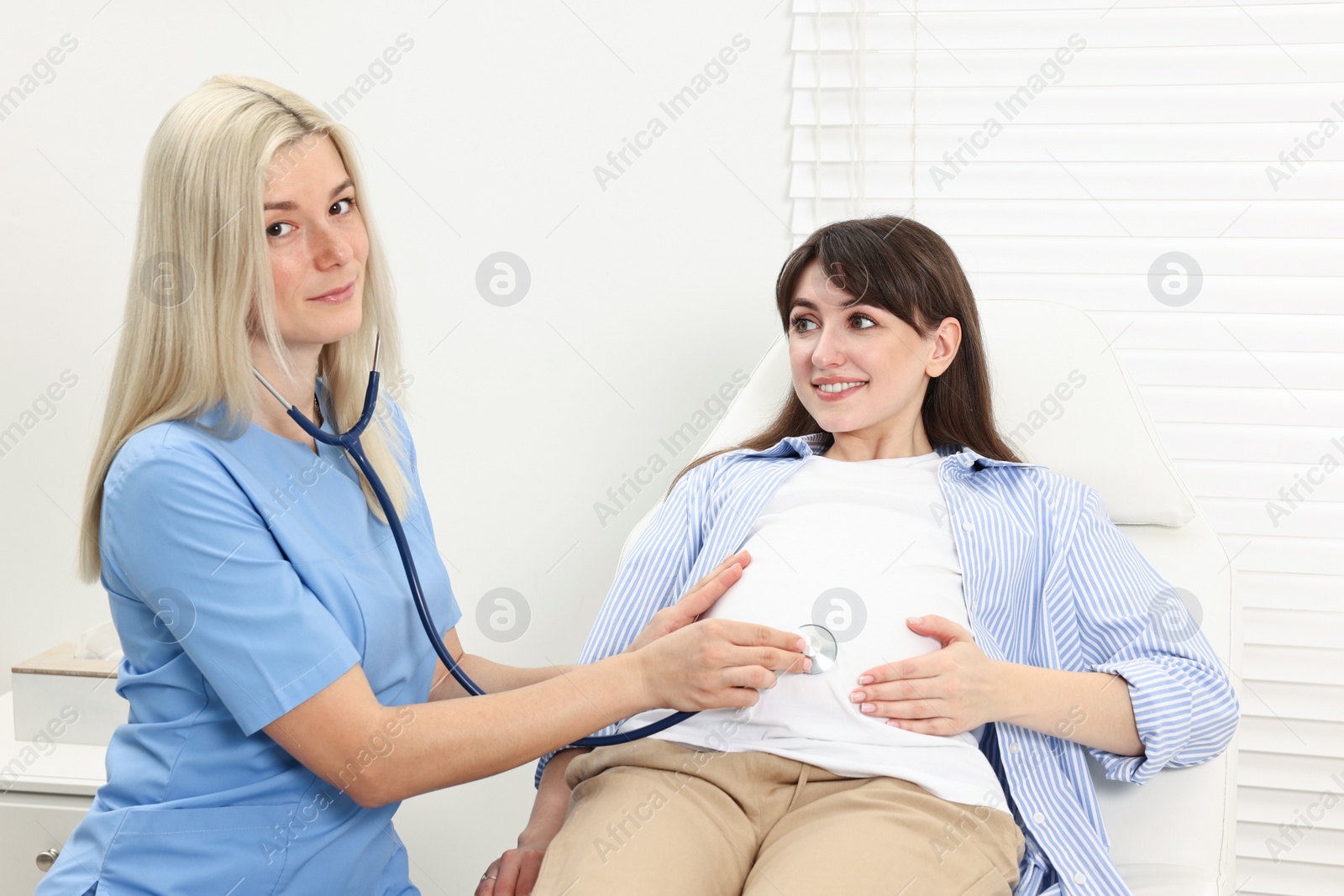 Photo of Pregnancy checkup. Doctor with stethoscope listening baby's heartbeat in patient's tummy in clinic