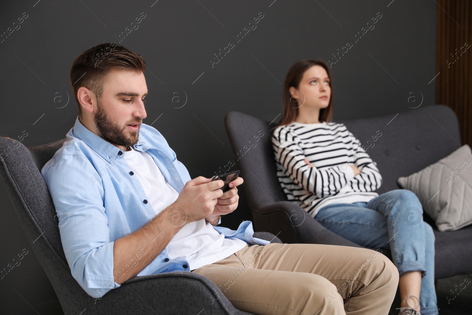 Photo of Young man preferring smartphone over his girlfriend at home. Relationship problems