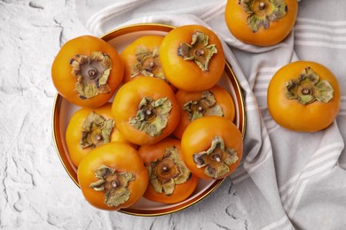 Bowl with delicious ripe juicy persimmons on white textured table, flat lay