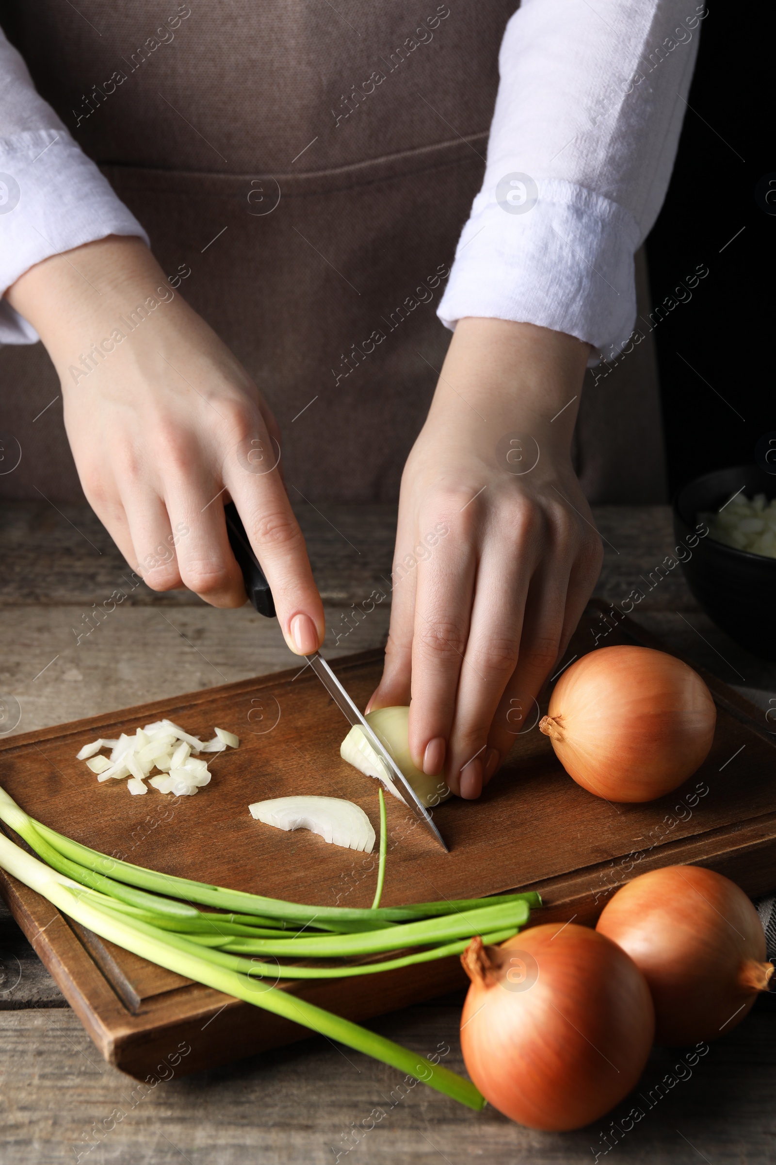 Photo of Woman cutting ripe onion at wooden table, closeup