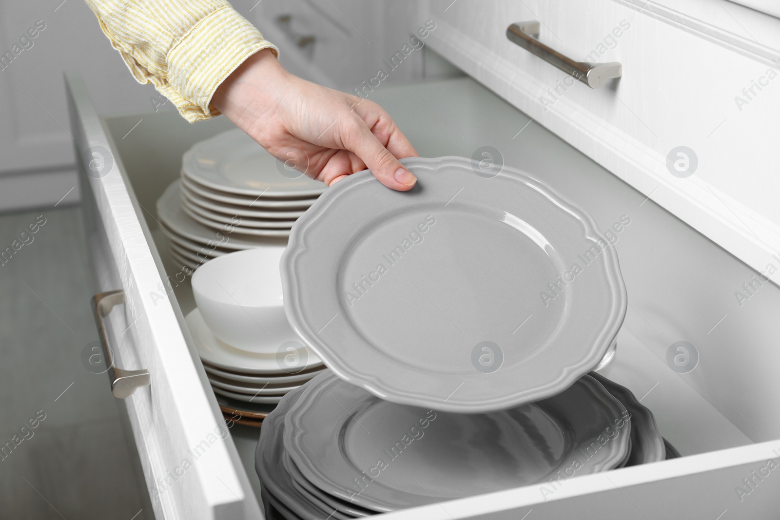 Photo of Woman taking grey plate from open drawer in kitchen, closeup
