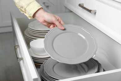 Photo of Woman taking grey plate from open drawer in kitchen, closeup