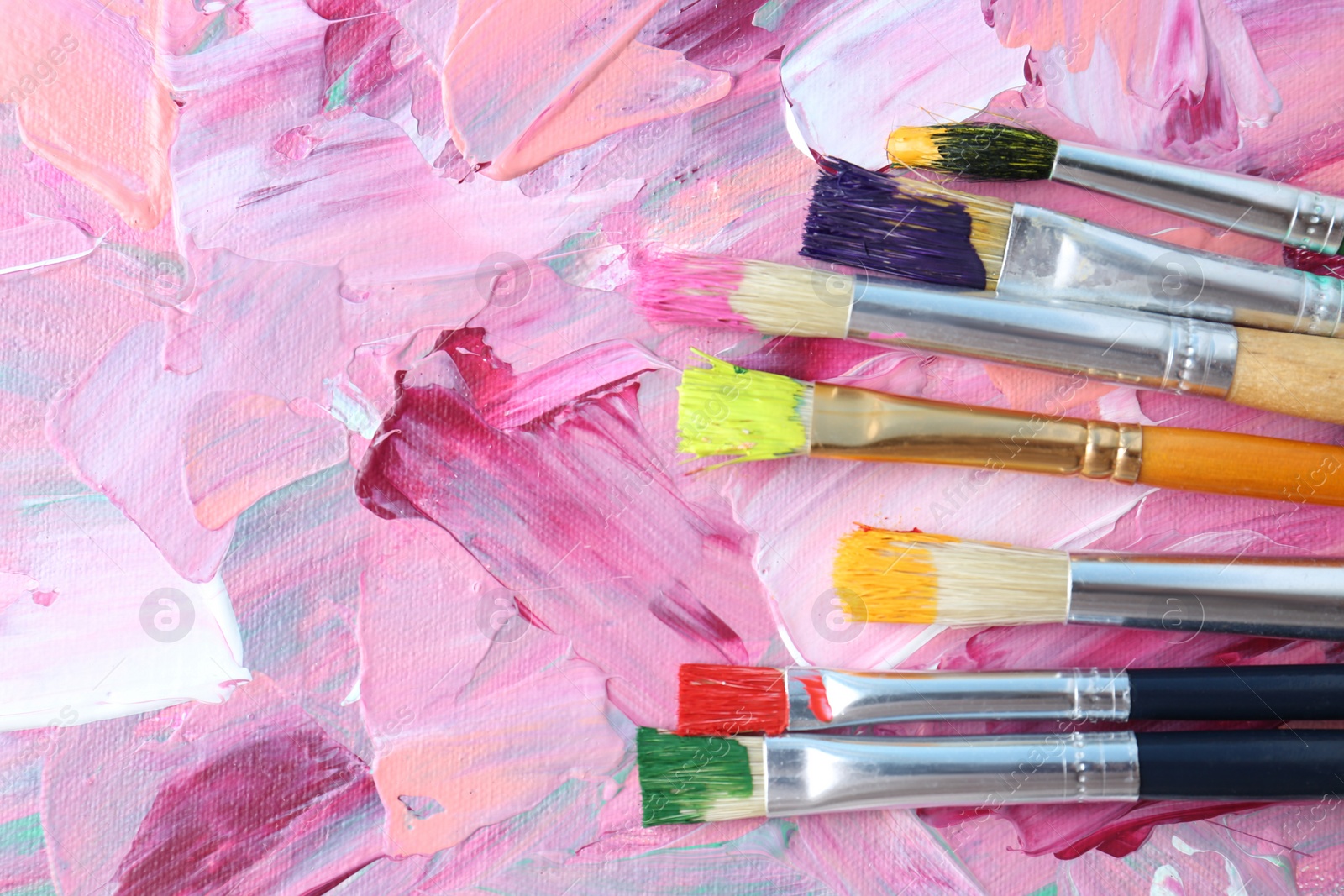 Photo of Set of different brushes on abstract colorful paint, flat lay