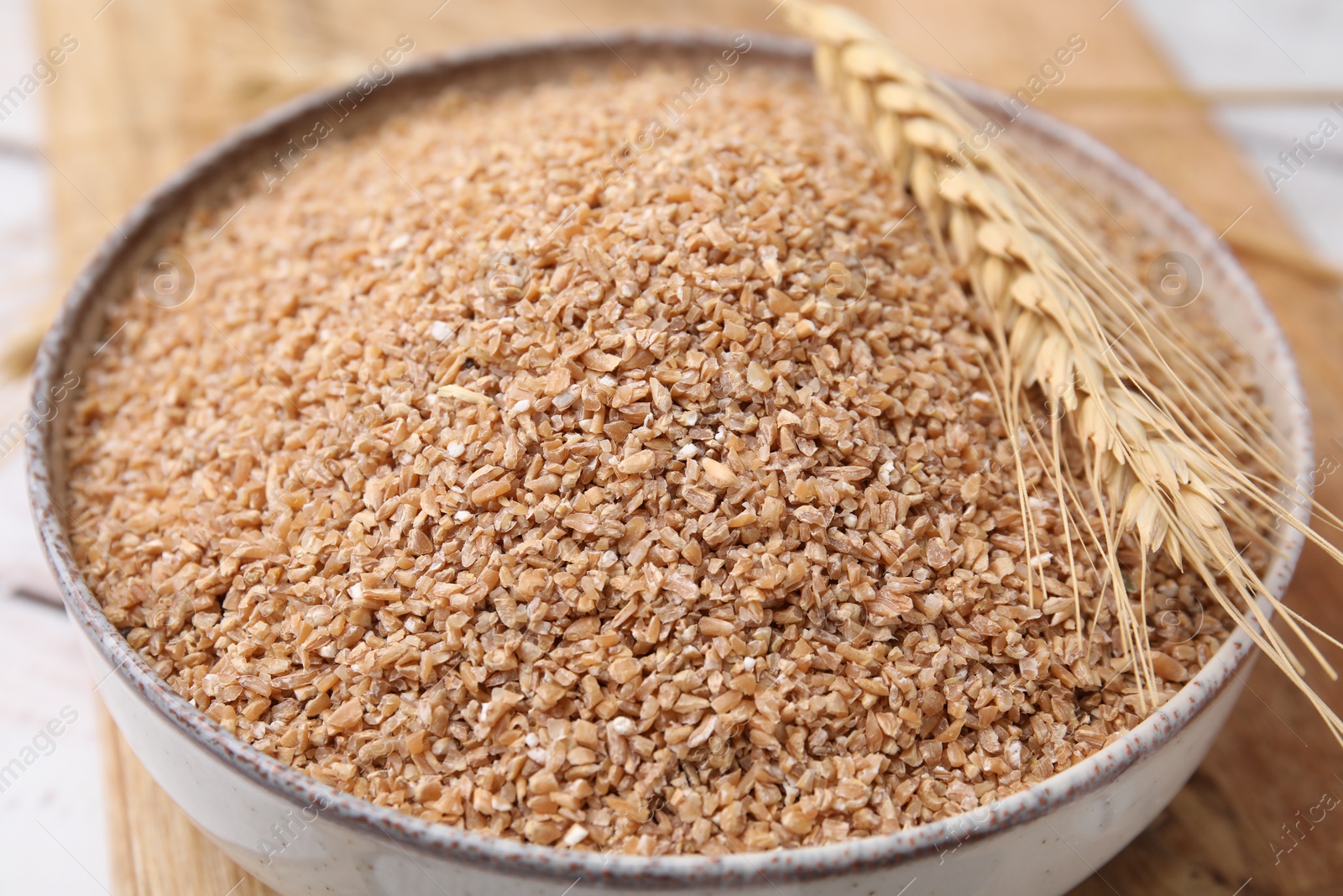 Photo of Dry wheat groats in bowl and spikelet on table, closeup