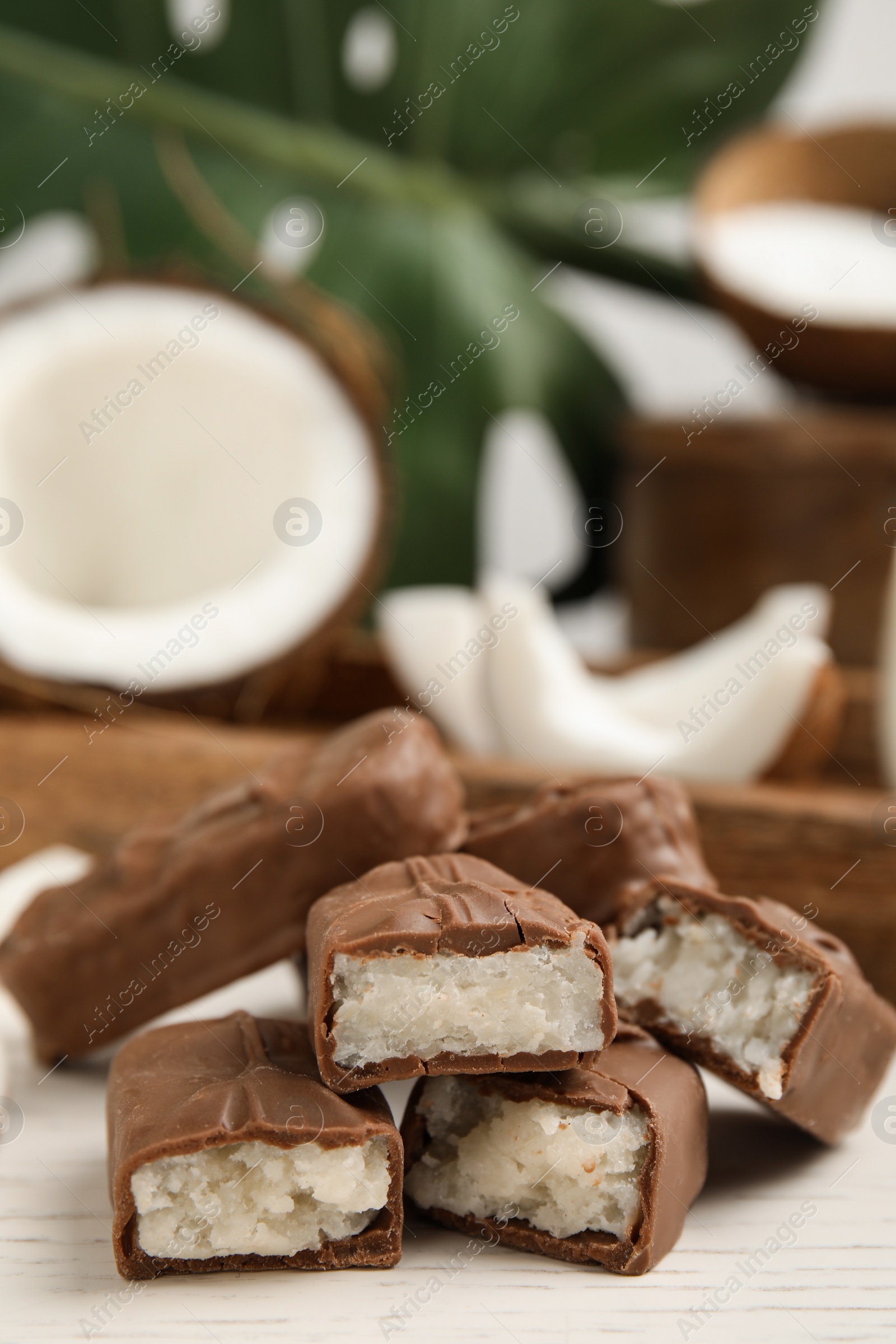 Photo of Delicious milk chocolate candy bars with coconut filling on white wooden table, closeup. Space for text