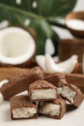 Photo of Delicious milk chocolate candy bars with coconut filling on white wooden table, closeup. Space for text