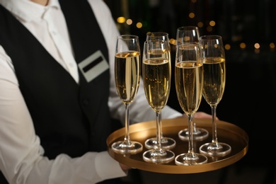 Photo of Waiter holding tray with glasses of champagne on blurred background, closeup
